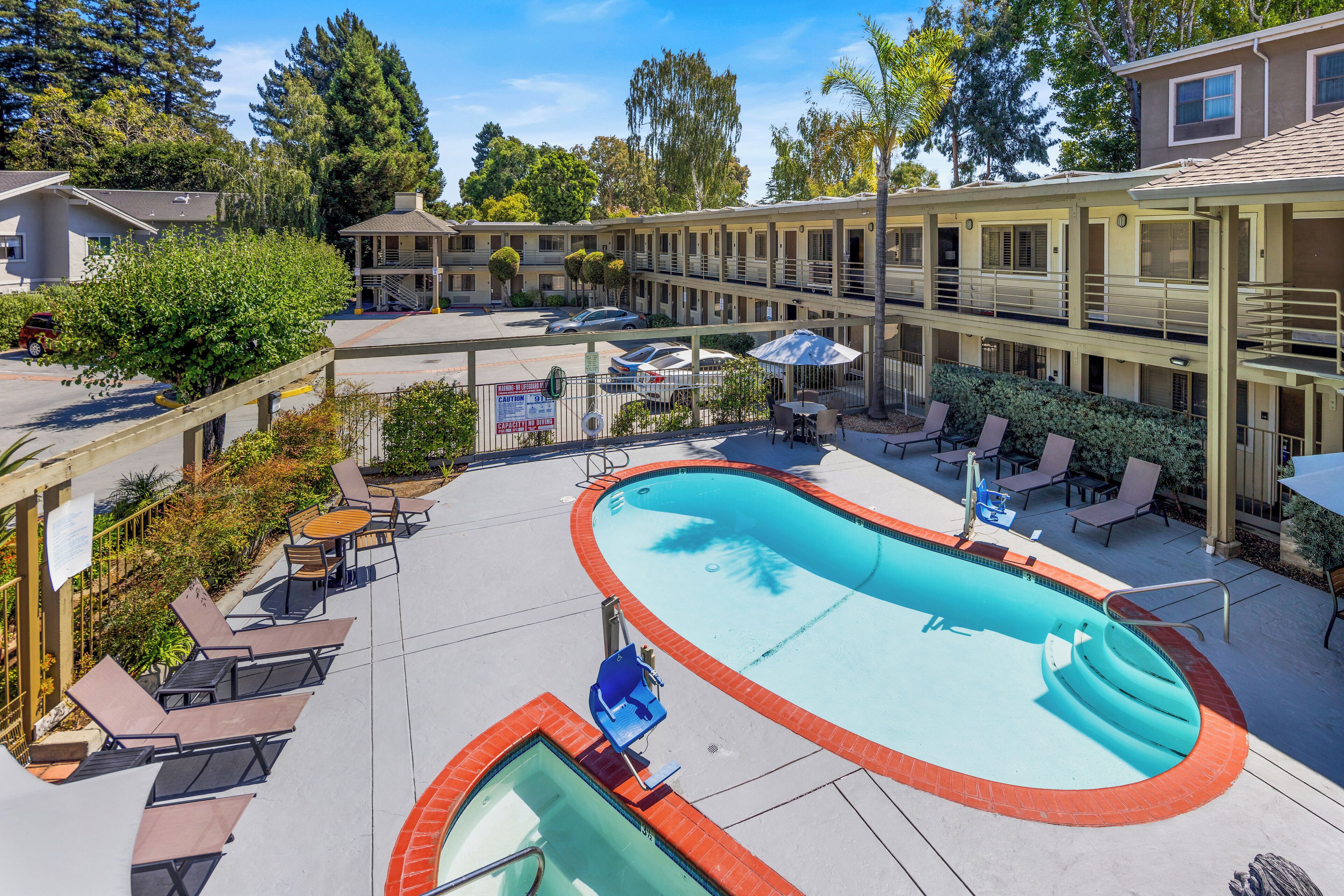 A hotel with a swimming pool, outdoor seating, and a parking area.