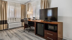 A hotel room with a wooden desk, a flat-screen TV, a microwave, a mini-fridge, a chair, a lamp, and a window with curtains. - Comfort Inn Santa Cruz North (Santa Cruz)