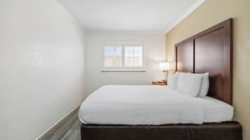 A hotel room with a bed, a nightstand, a lamp, and a window.