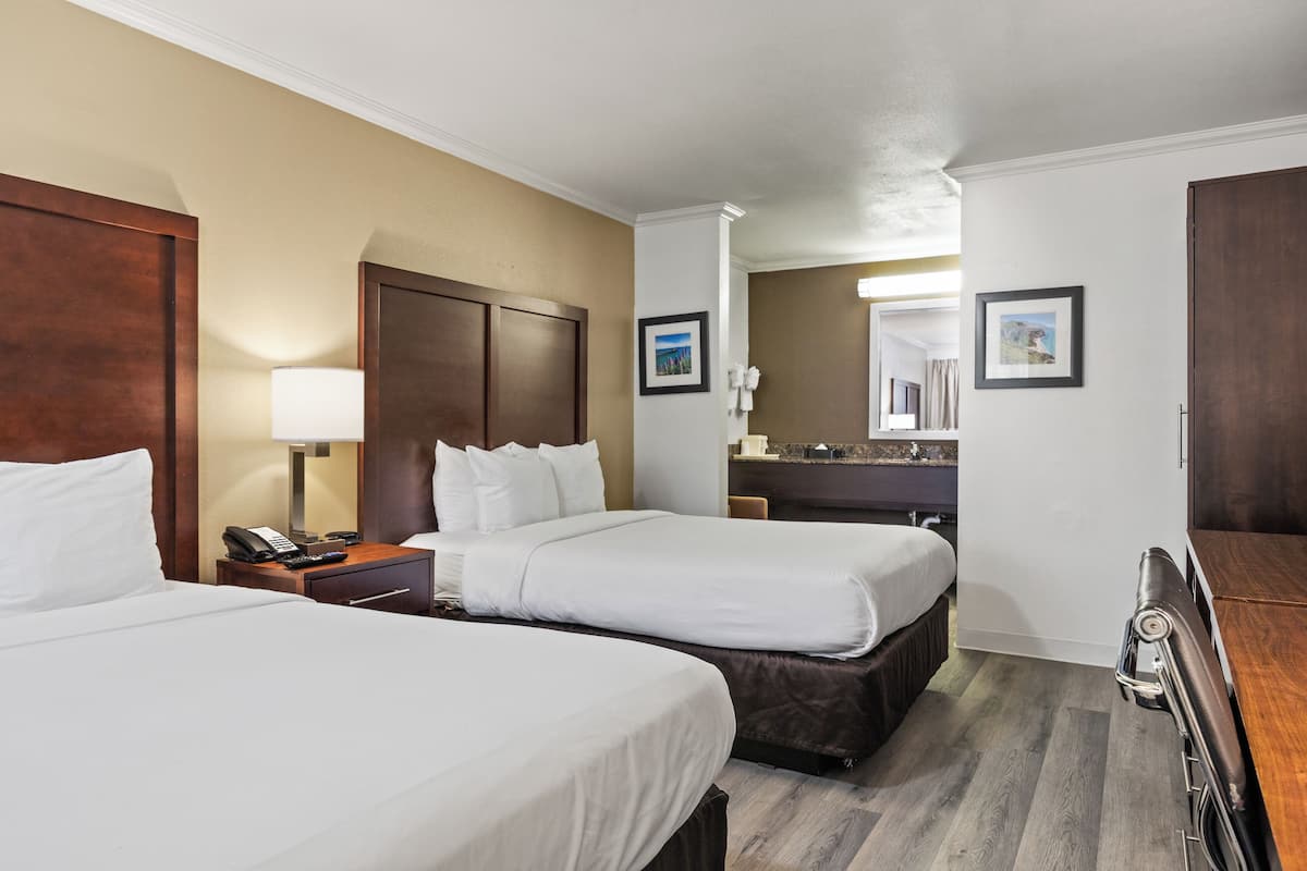 Ein Hotelzimmer mit zwei Betten, einem Schreibtisch mit Lampe, einem Spiegel und einer Kommode.