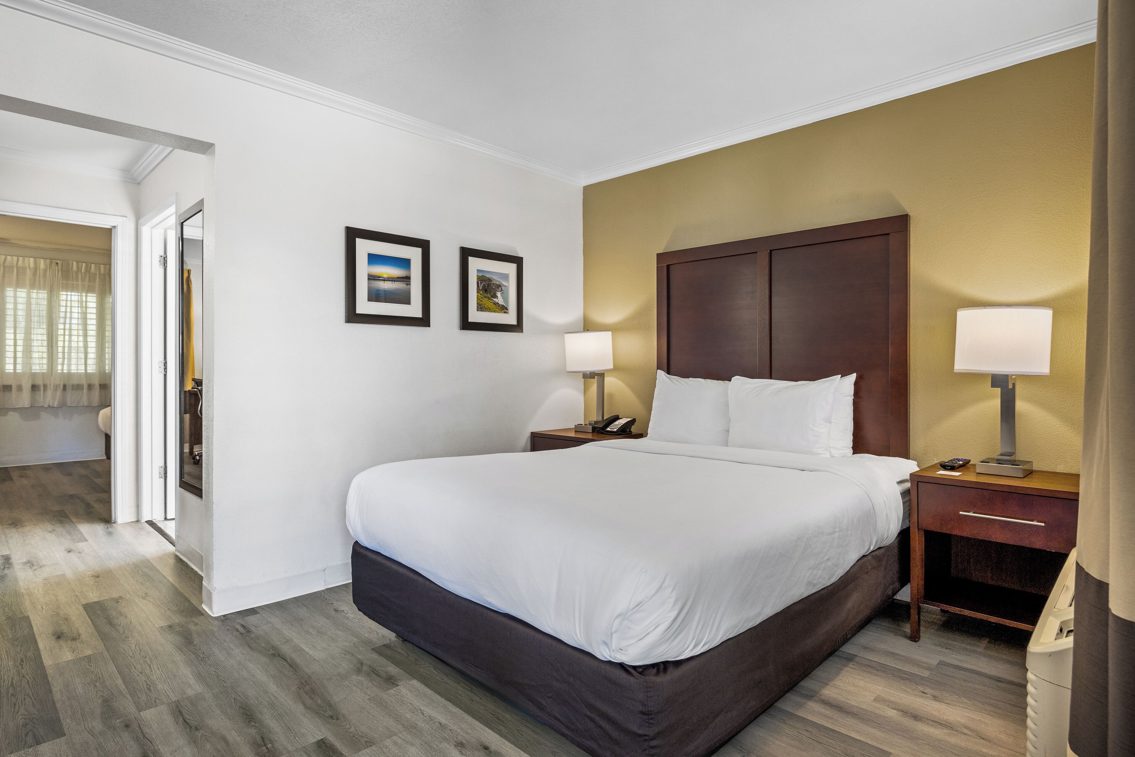 A hotel room with a large bed, two bedside tables, a nightstand, a lamp, and two framed pictures on the wall.