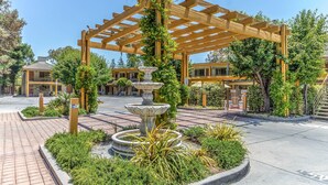 A wooden pergola with climbing plants, a central fountain, and a paved walkway leading to a building entrance. - Comfort Inn Santa Cruz North (Santa Cruz)