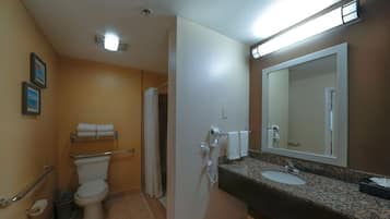 Ein Badezimmer mit Toilette, Waschbecken und Spiegel. Darüber hängt ein Handtuchhalter über der Toilette und ein Fön ist an der Wand befestigt.