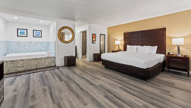 A hotel room with a large bed, a bathroom with a bathtub, and a wooden floor. - Comfort Inn Santa Cruz North (Santa Cruz)