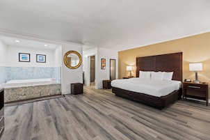 Una habitación de hotel con una cama grande, un baño con bañera y suelo de madera.