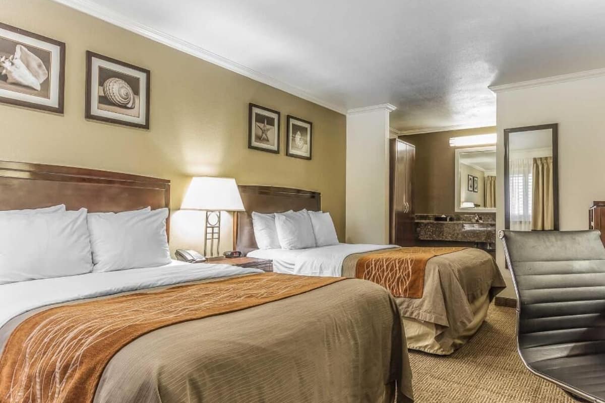 Ein Hotelzimmer mit zwei Betten, einem Sessel, einem Schreibtisch und einem Spiegel.