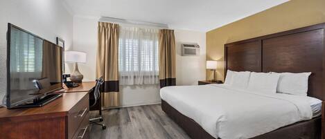 Habitación de hotel con una cama grande, un escritorio con televisor de pantalla plana, una lámpara y una ventana con cortinas.