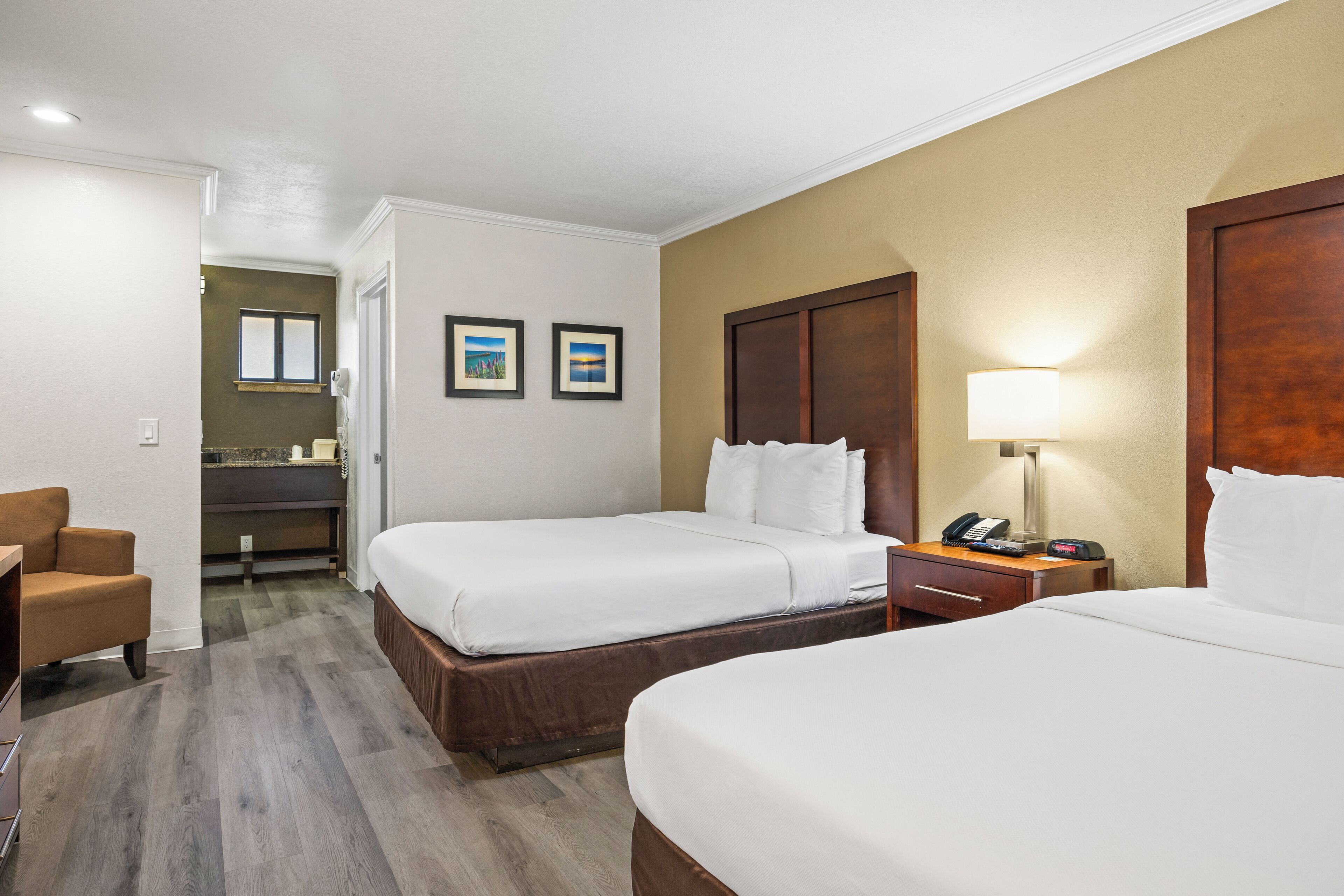 Ein Hotelzimmer mit zwei Betten, einem Schreibtisch mit Lampe, einem Stuhl und einem durchgegangenen Tür zugehörigen Badezimmer.
