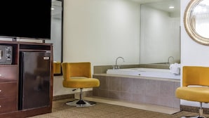 A bathroom with a large mirror, a bathtub, two yellow chairs, and a television on a cabinet. - Comfort Inn Santa Cruz North (Santa Cruz)