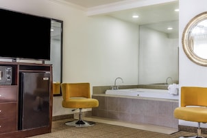 Un baño con un espejo grande, una bañera, dos sillas amarillas y un televisor sobre un mueble.