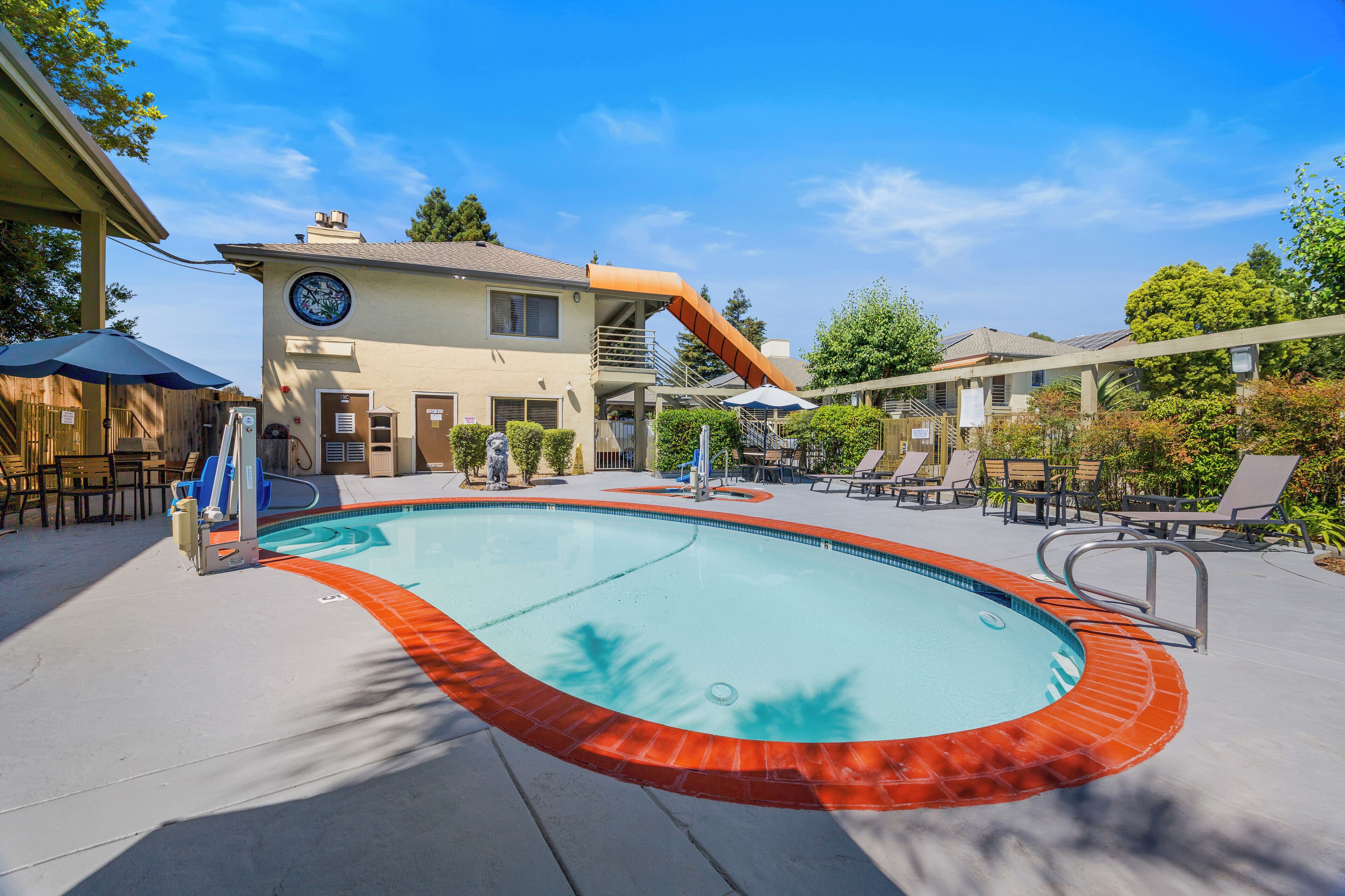 A swimming pool with a red border, a water slide, and lounge chairs.