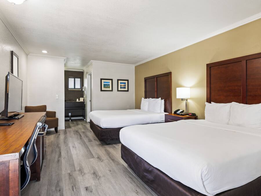 A hotel room with two beds, a desk, a chair, a lamp, and a TV.
