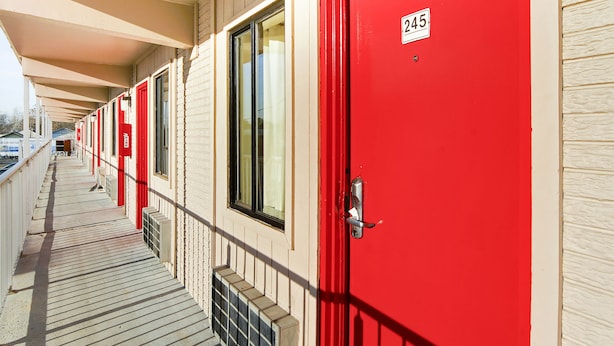 A row of red doors with a number plate, a covered walkway, and a building facade. - OYO Hotel Petersburg VA I-95 & E Washington St (Petersburg)