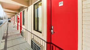 A row of red doors with a number plate, a covered walkway, and a building facade.