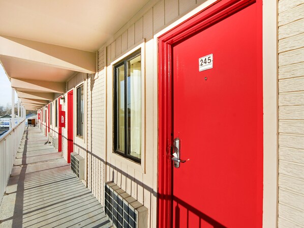 A row of red doors with a number plate, a covered walkway, and a building facade. - OYO Hotel Petersburg VA I-95 & E Washington St (Petersburg)