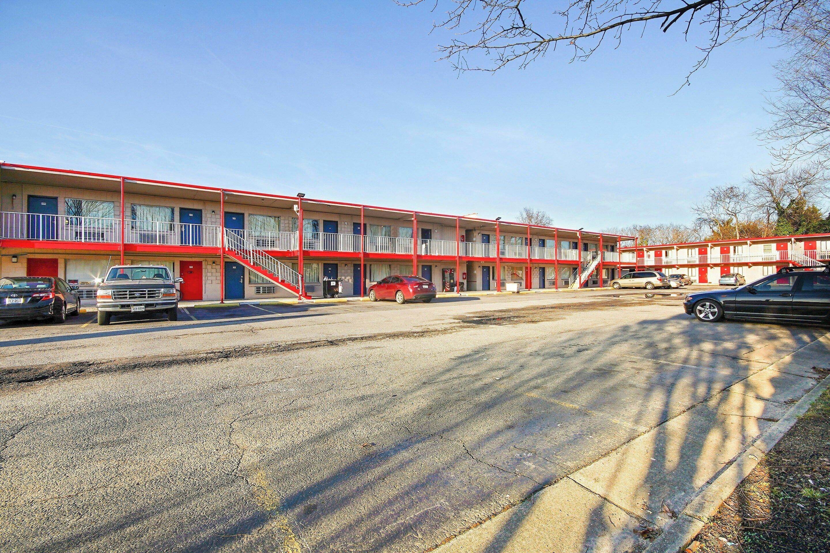A motel with multiple floors, a parking lot, and a red car parked in front.