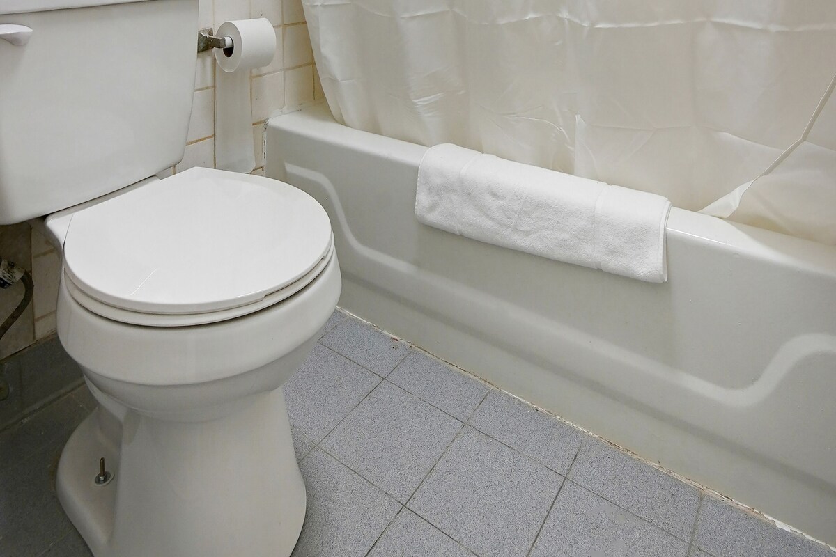 A bathroom with a toilet, a roll of toilet paper, a bathtub with a white towel, and tiled flooring.