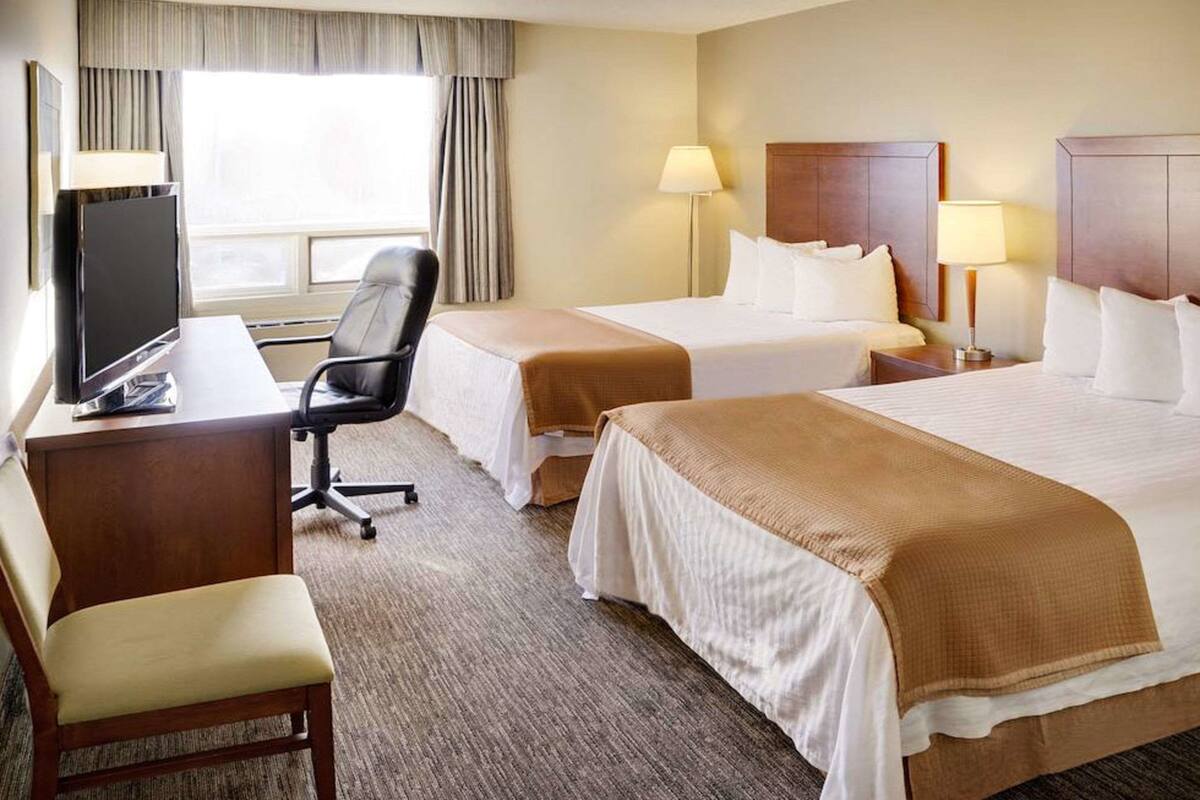 A hotel room with two beds, a desk with a computer, a chair, and a TV.