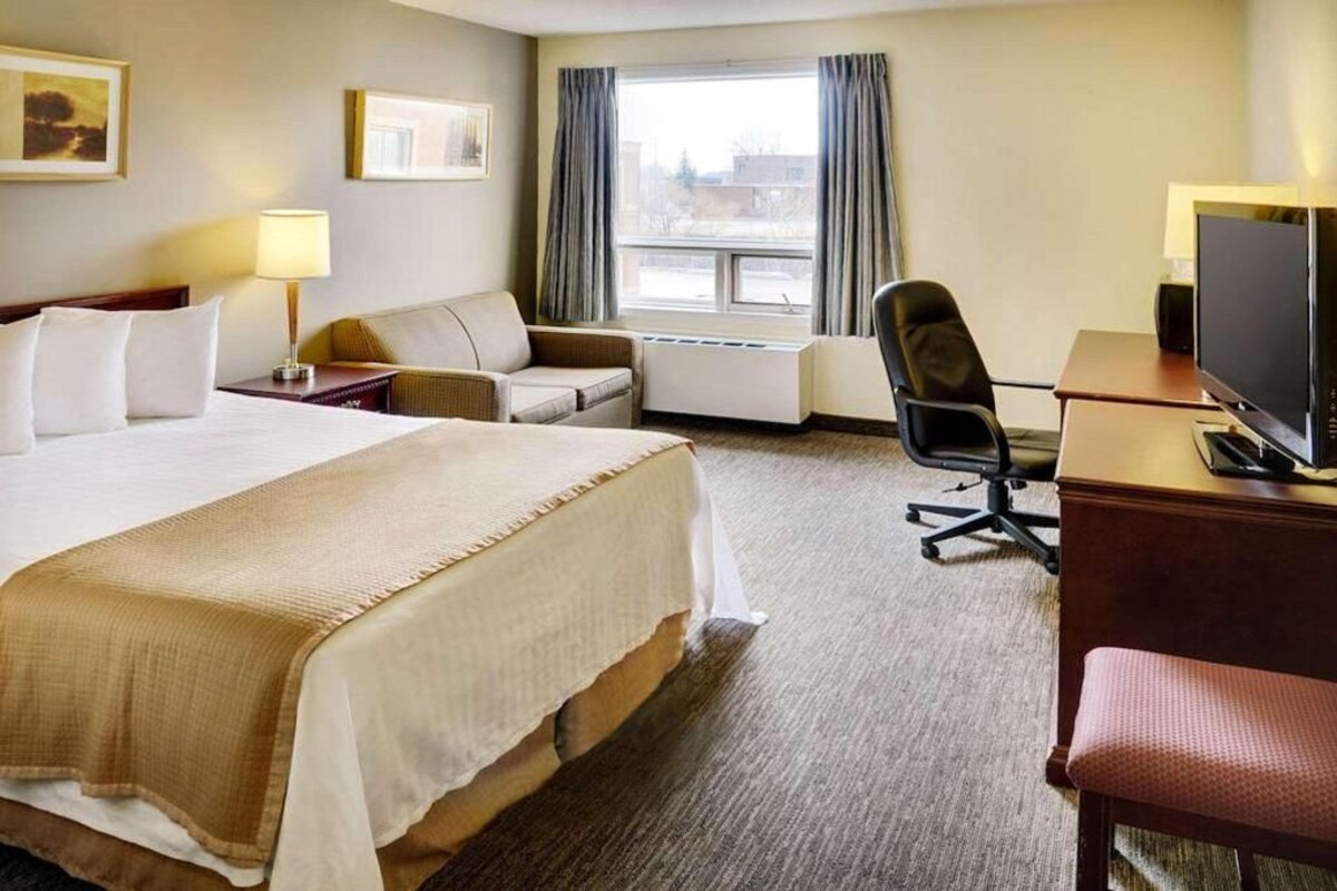 Une chambre d’hôtel avec un grand lit, un bureau avec un ordinateur, une chaise, un canapé et une fenêtre avec des rideaux.