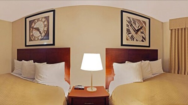 A hotel room with two beds, a nightstand with a lamp, and two clocks on the walls.