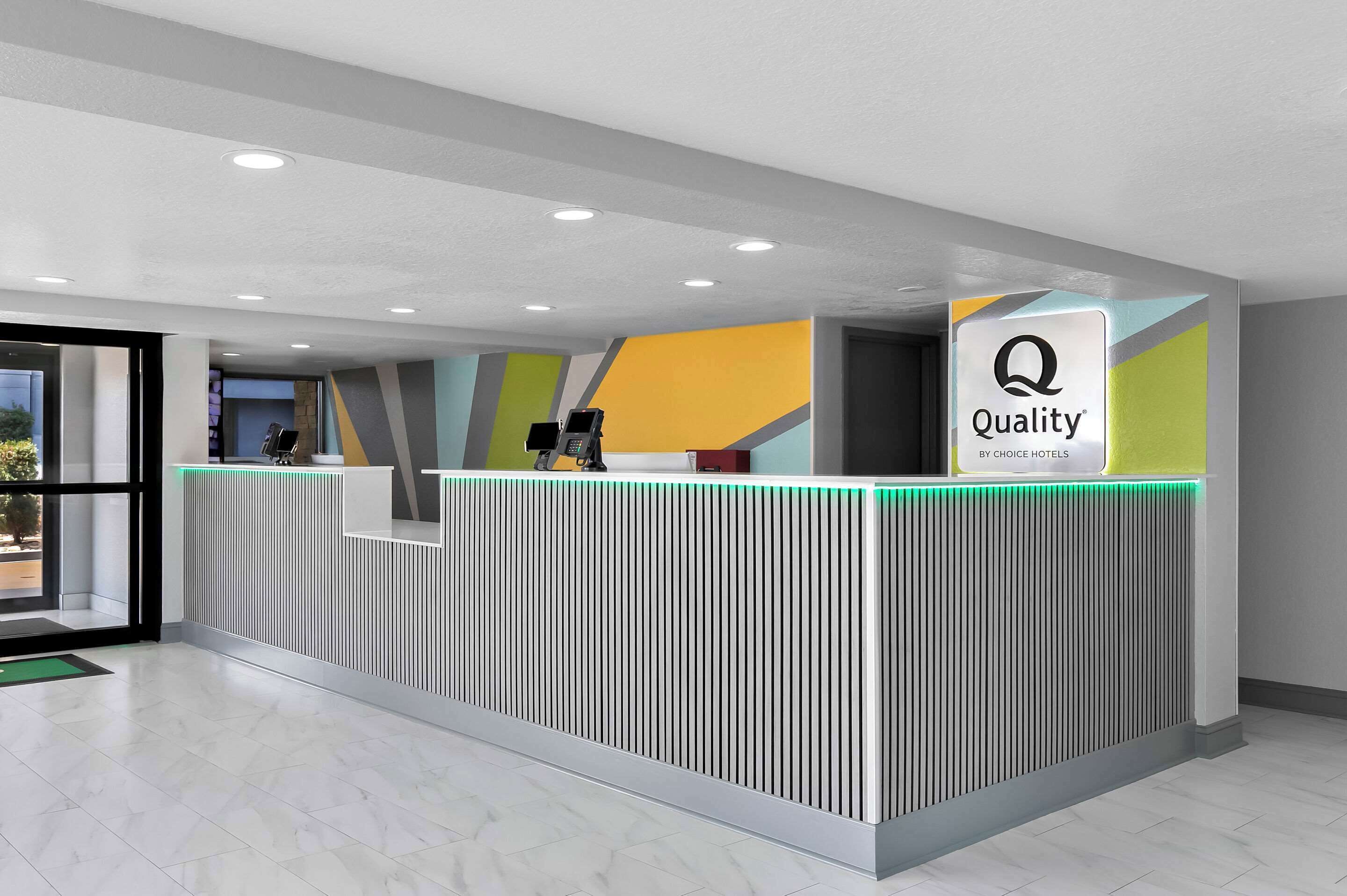 Una recepción de hotel de diseño moderno, con paneles verticales y un letrero que dice 'Quality by Choice Hotels'.