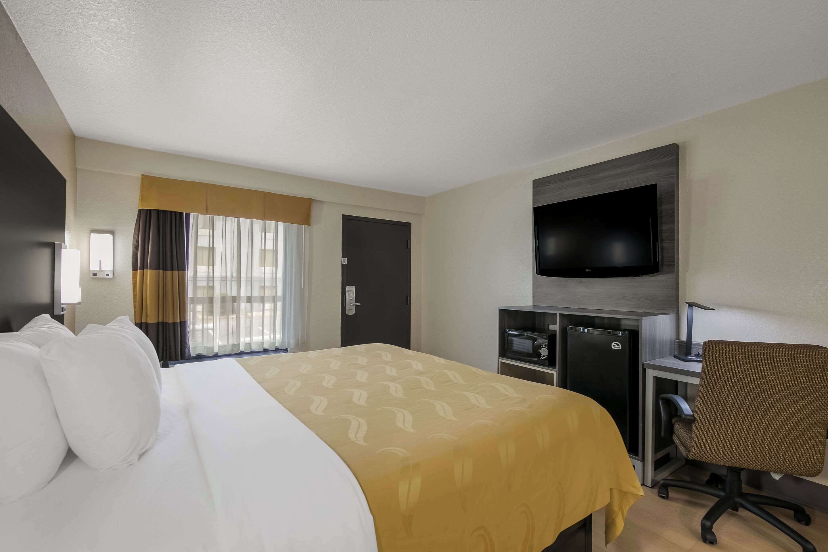 A hotel room with a bed, a desk, a chair, a television, and a minibar.