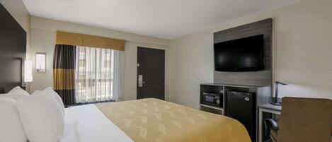 A hotel room with a bed, a desk, a chair, a television, and a minibar.
