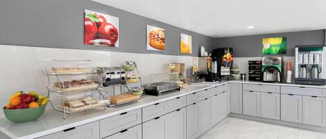 Una cocina moderna con encimera de mármol, frutero, estación para café y decoración en la pared.