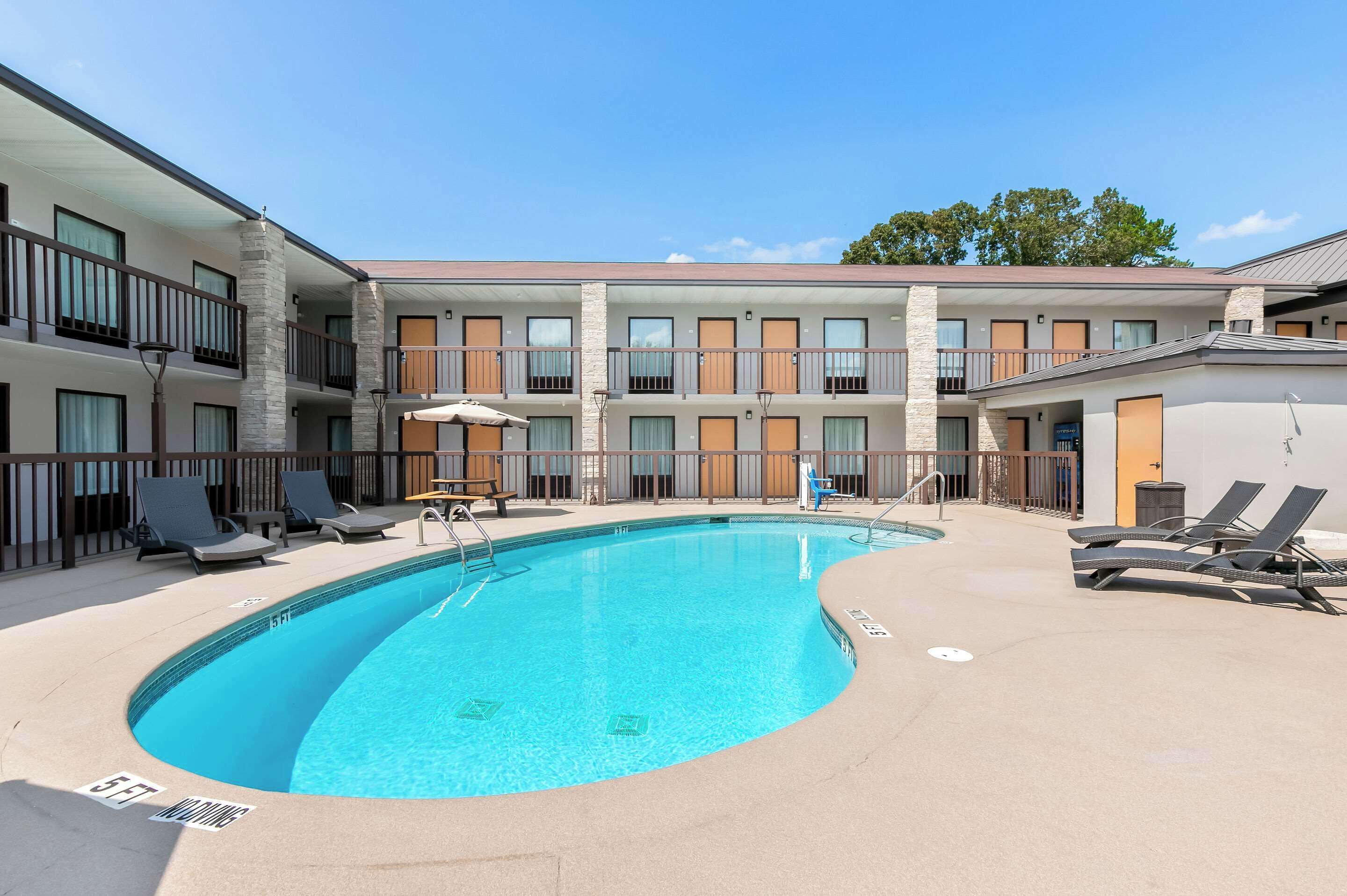 A hotel with a swimming pool, sun loungers, and a covered seating area.