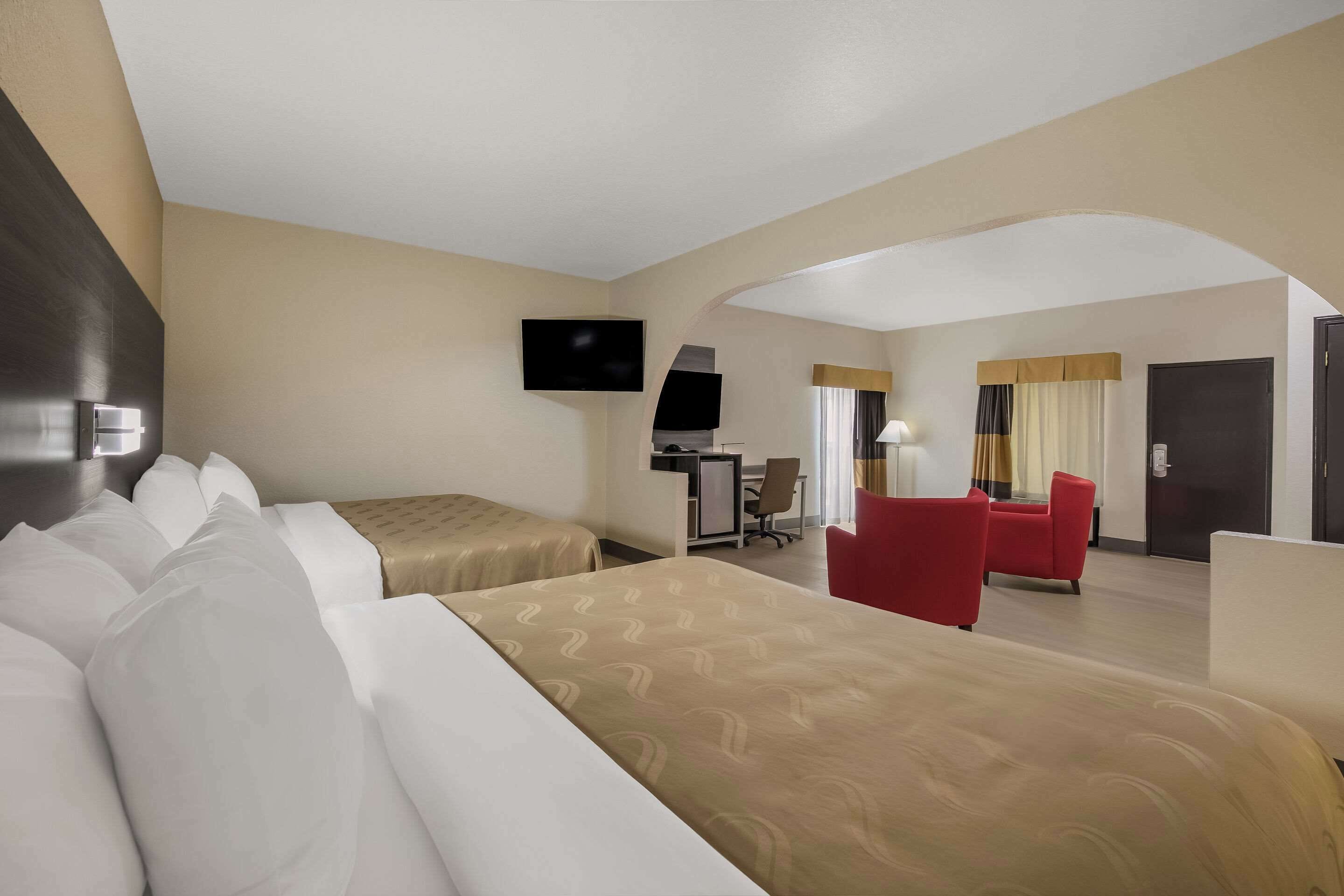 Quarto de hotel com duas camas, uma mesa, uma televisão e uma cadeira vermelha.