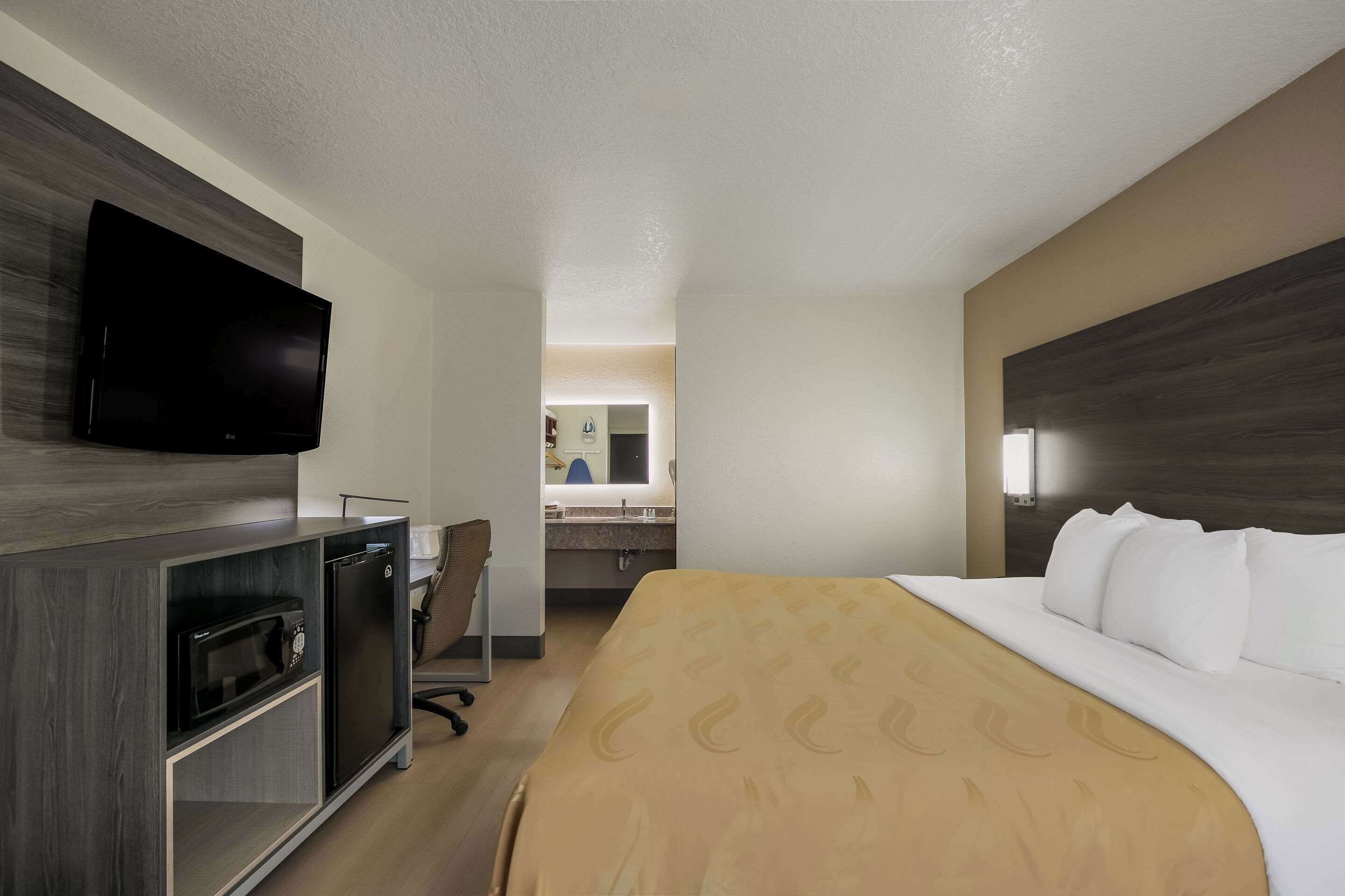A hotel room with a bed, a television mounted on the wall, a microwave, and a refrigerator.