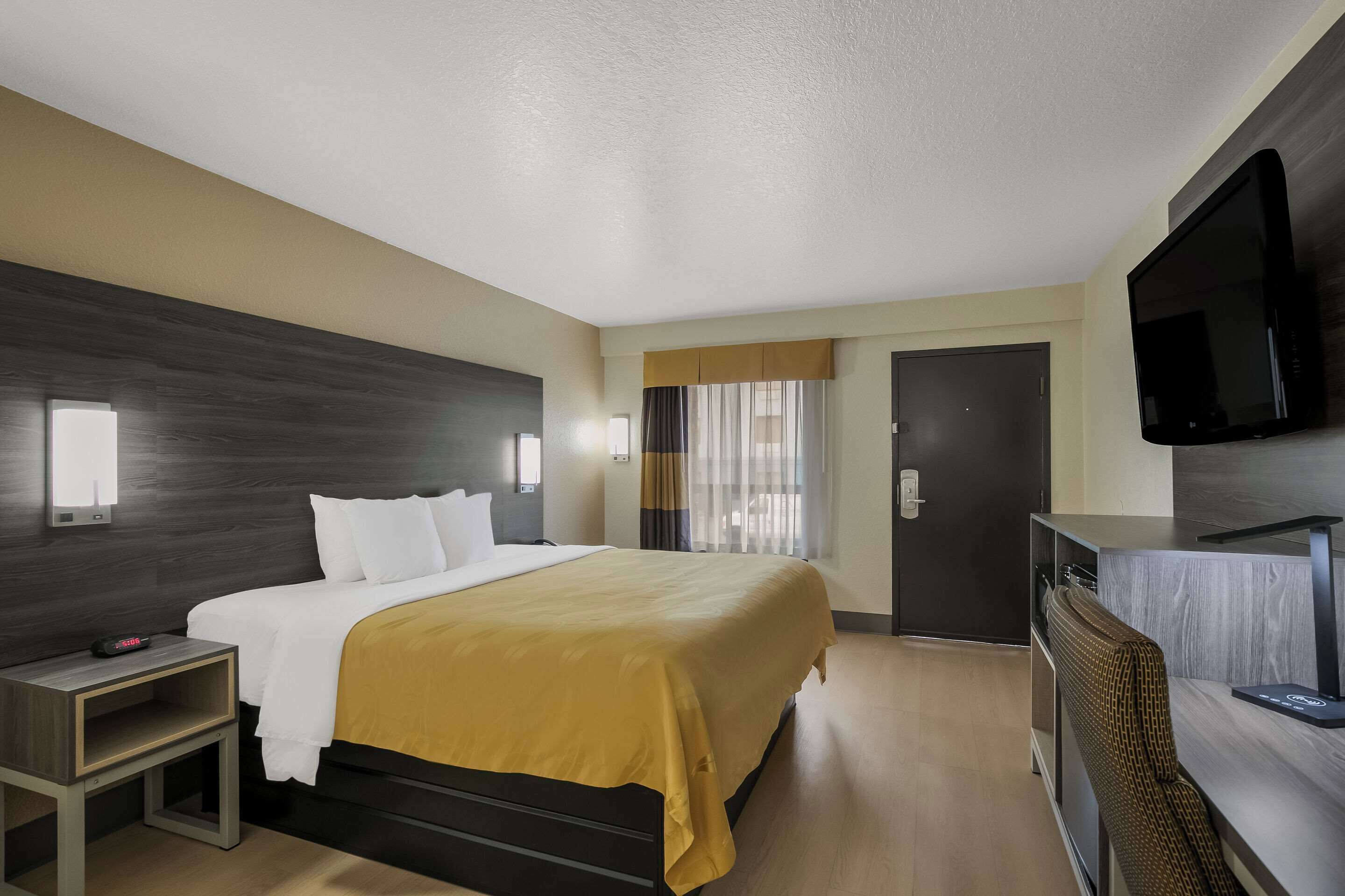 Une chambre d’hôtel avec un lit, une table de chevet, une télévision et un bureau.