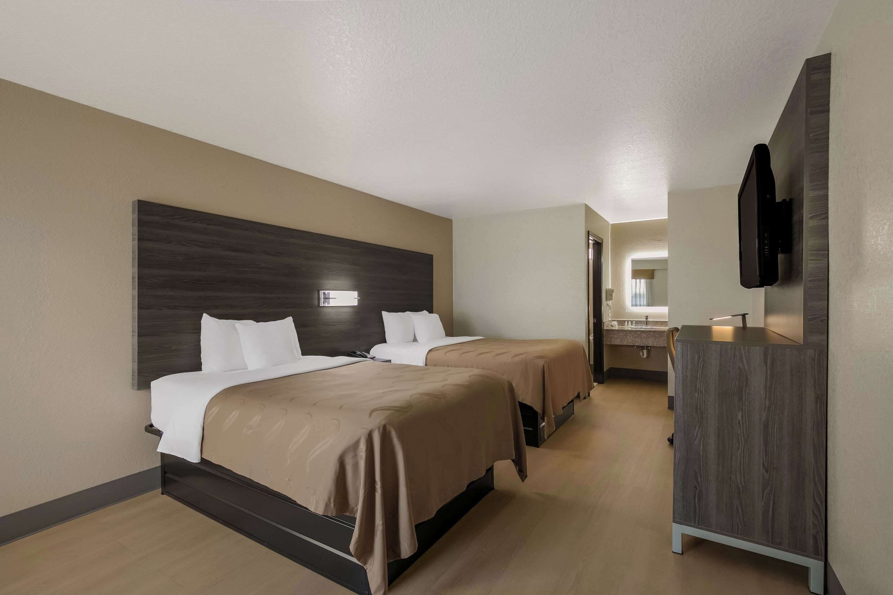 Habitación de hotel con dos camas, cabecero de madera, televisor de pantalla plana montado en la pared y cómoda de madera.