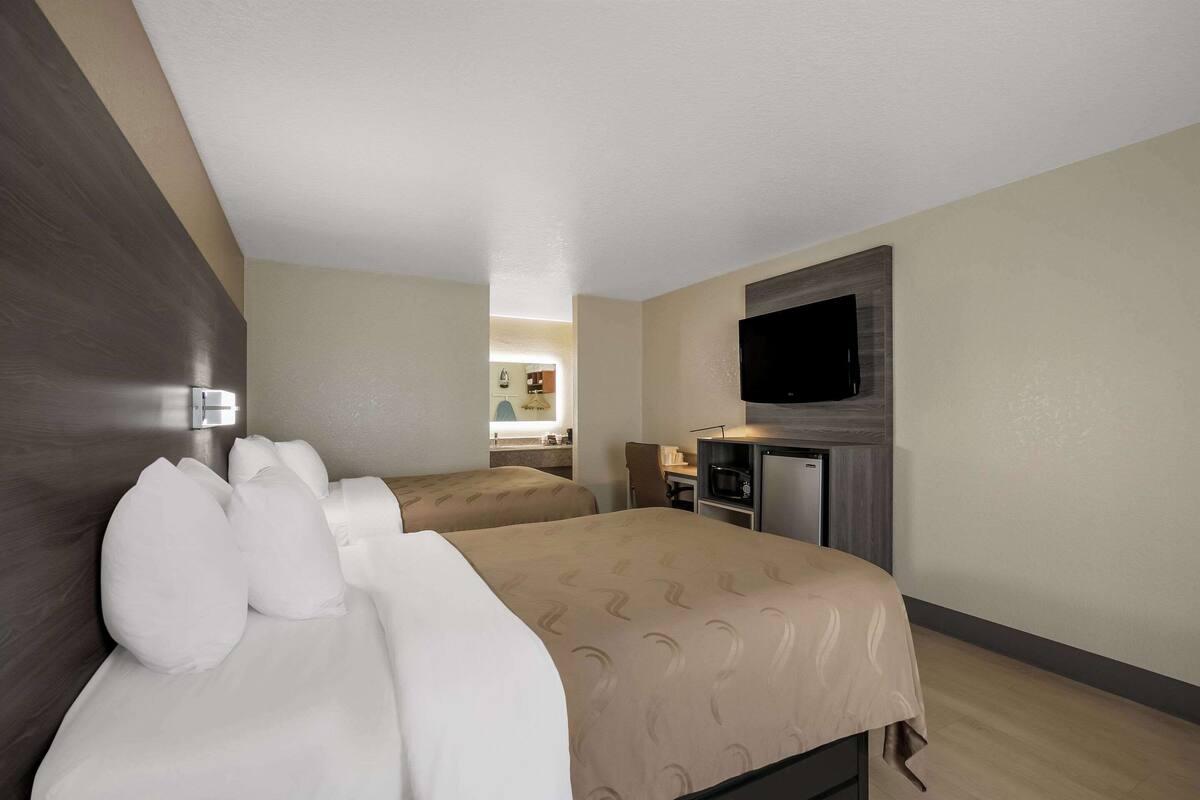 A hotel room with two beds, a TV, a desk, and a kitchenette.