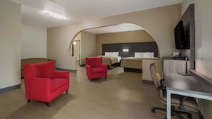 Ein Hotelzimmer mit rotem Sessel, Schreibtisch mit Stuhl, Bett mit Kopfteil und Wand-Fernseher.