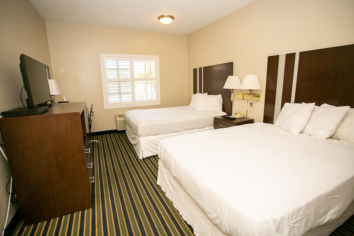 A hotel room with two beds, a desk with a computer, a TV, and a window with blinds.