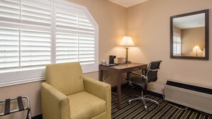 A hotel room with a yellow armchair, a desk with a lamp, a chair, a radiator, and a window with blinds. - Travel Inn (Sunnyvale)