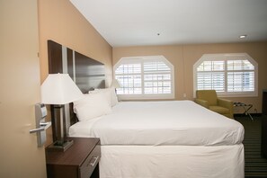 A hotel room with a large bed, two bedside lamps, a chair, and a window with blinds.