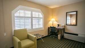 A hotel room with a striped carpet, a green armchair, a desk with a lamp, a chair, and a radiator. - Travel Inn (Sunnyvale)