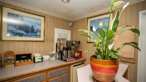 A hotel reception area with a wooden counter, a coffee machine, a small refrigerator, and a potted plant. - Travel Inn (Sunnyvale)