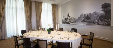 A dining room with a round table set for six, surrounded by chairs, with a large wall mural depicting a landscape scene.