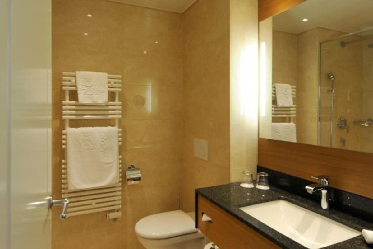 A bathroom with a toilet, sink, mirror, towel rack, and shower.