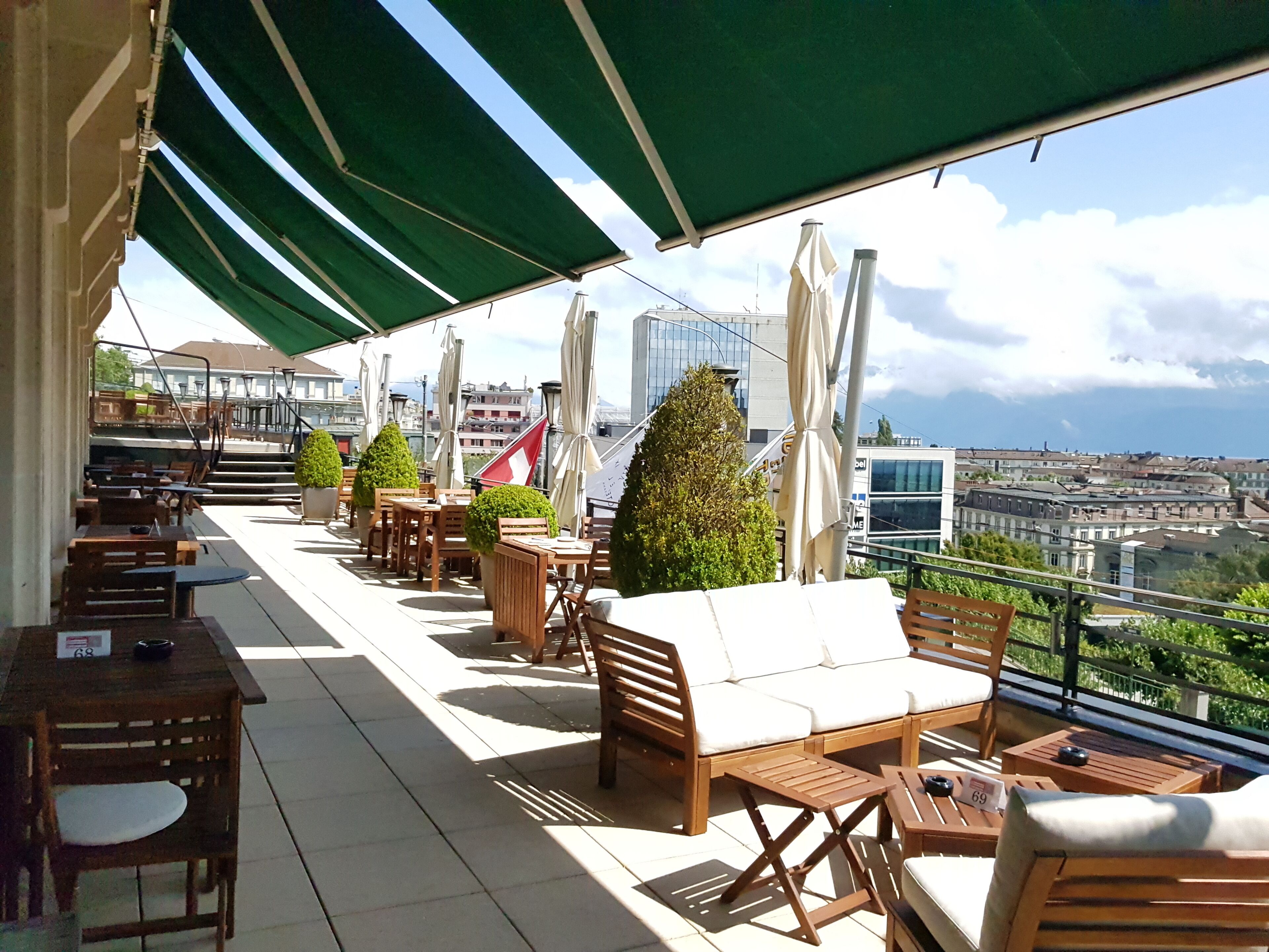 Una terraza en la azotea con mobiliario de madera, incluyendo mesas y sillas, bajo toldos verdes.