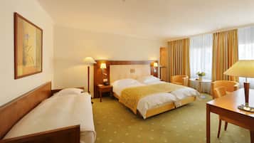 A hotel room with a large bed, two bedside tables with lamps, a small round table with a chair, and a painting on the wall.