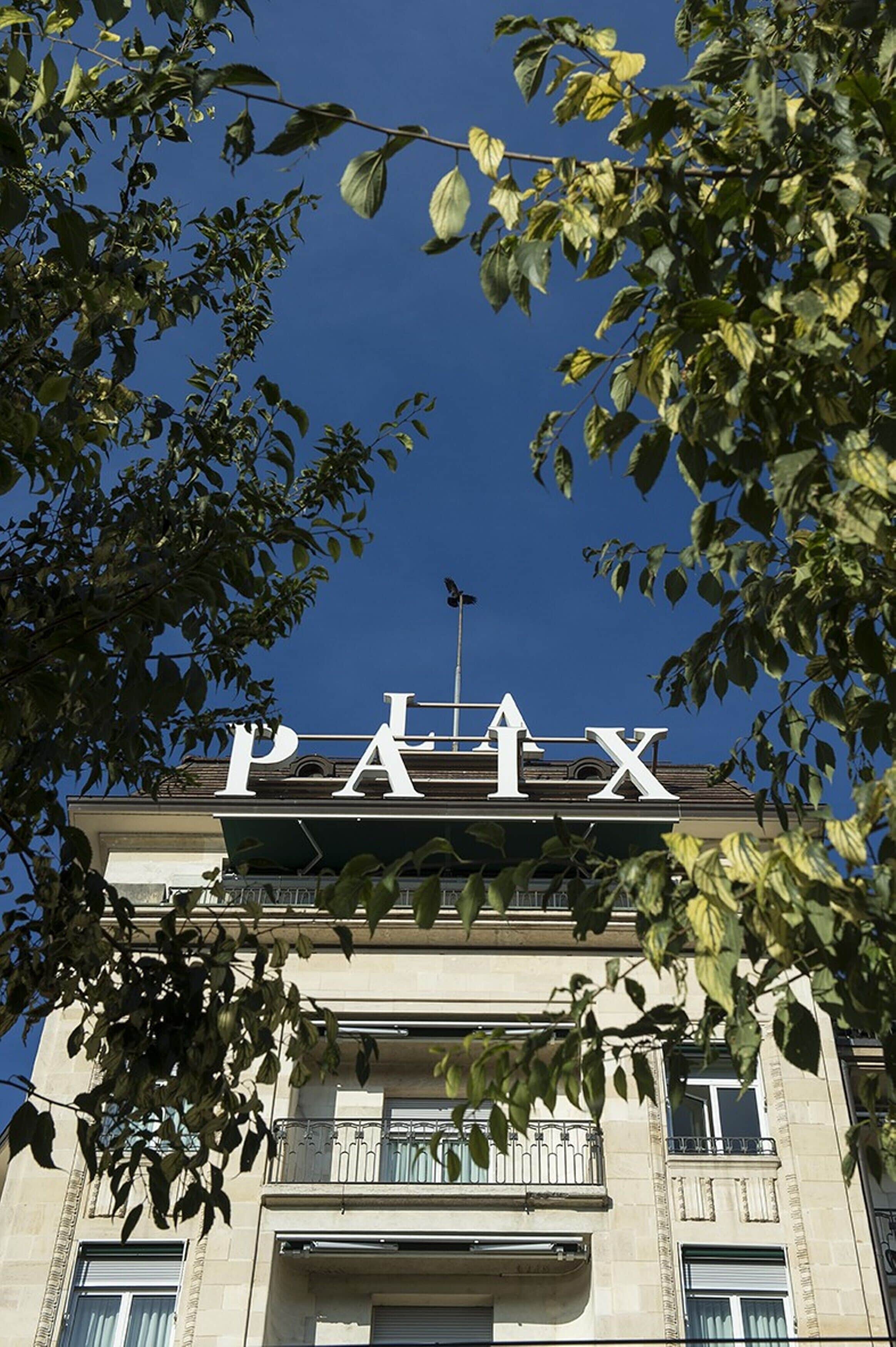 A building with the sign "PAIX" on the facade, surrounded by trees.