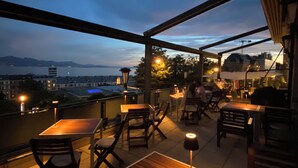 An outdoor patio with wooden tables and chairs, a view of the cityscape, and a body of water in the distance. - De la Paix (Lausanne)