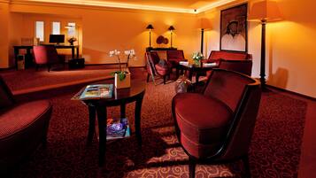 Ein Hotelzimmer mit rotem Teppich, einem Schreibtisch mit Computer, zwei Stühlen, einem Tisch mit Blumenvase und einer Lampe.