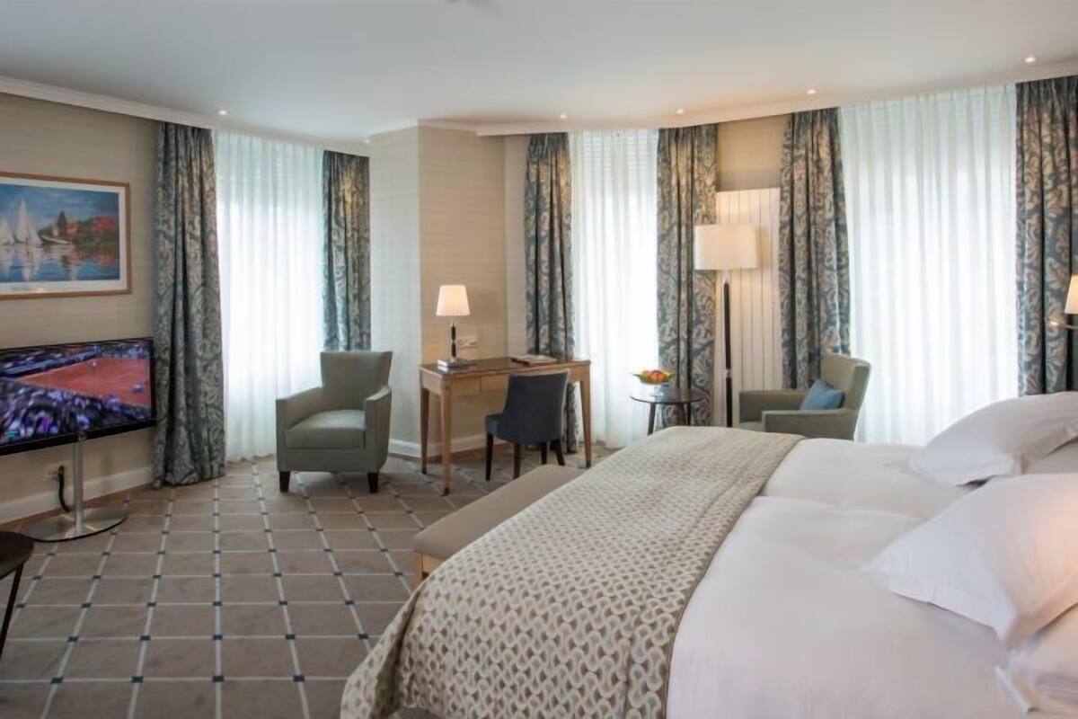 A hotel room with a bed, desk, chair, TV, and curtains.