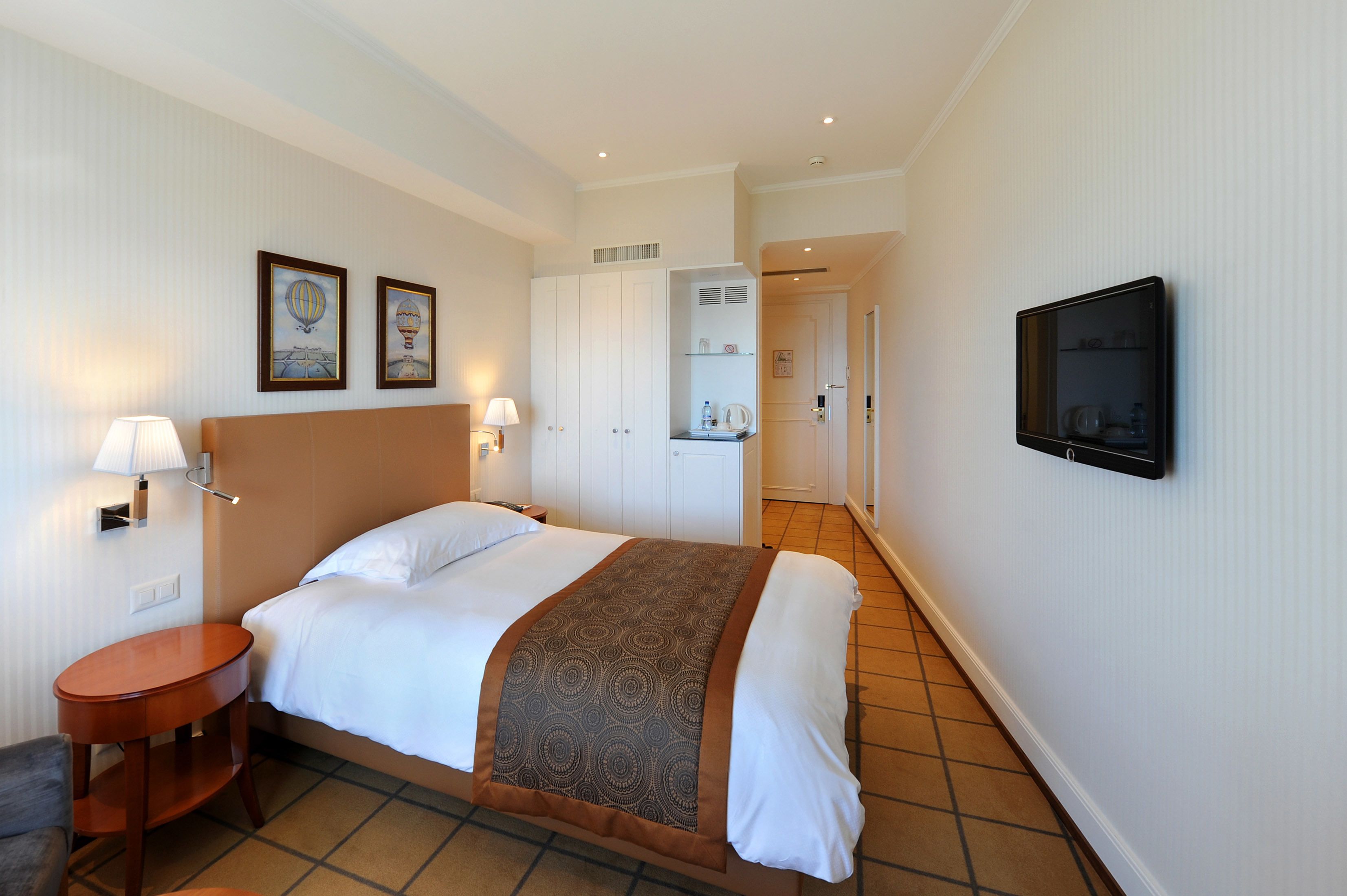 A hotel room with a bed, bedside tables, a TV, and a bathroom visible through an open door.