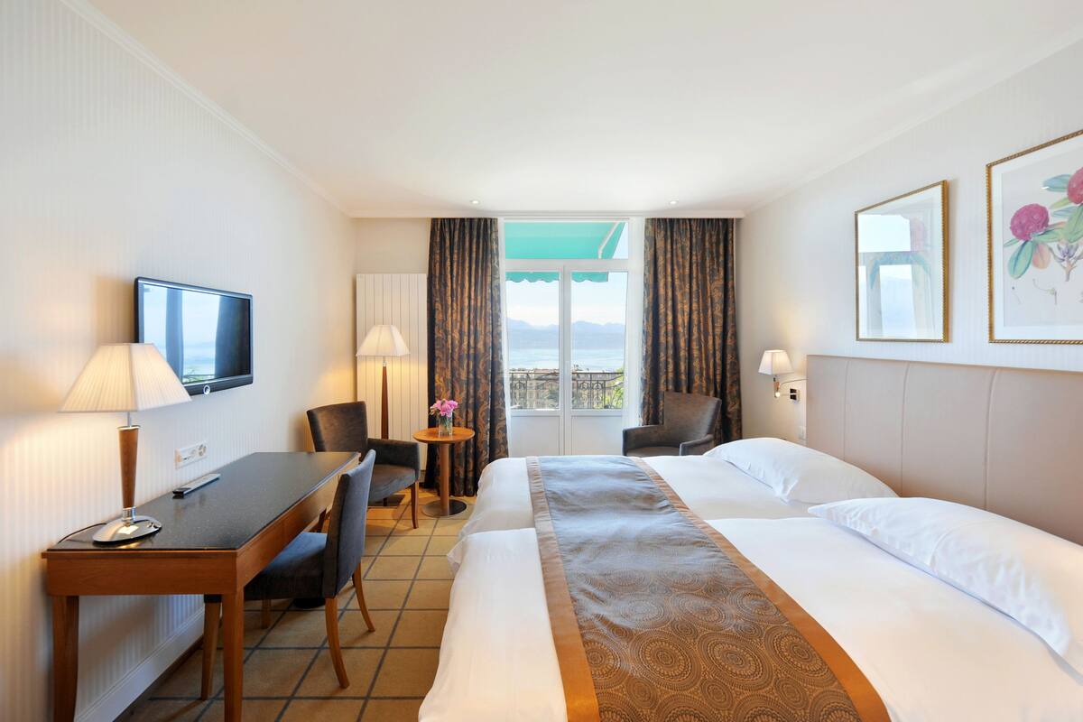 A hotel room with a bed, a desk, a chair, a TV, and a window with curtains.